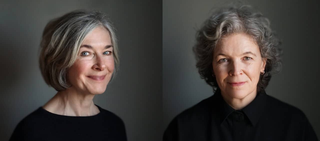 Side-by-side portraits of two women in soft, natural light against a grey background. On the left, a woman with short grey hair and a gentle smile wears a black top. On the right, a woman with short curly grey hair and a calm, direct expression also wears a black top.