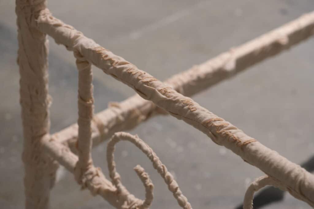 A detail of a bedframe wrapped in fabric which is embroidered with the phrase "There will be blood."