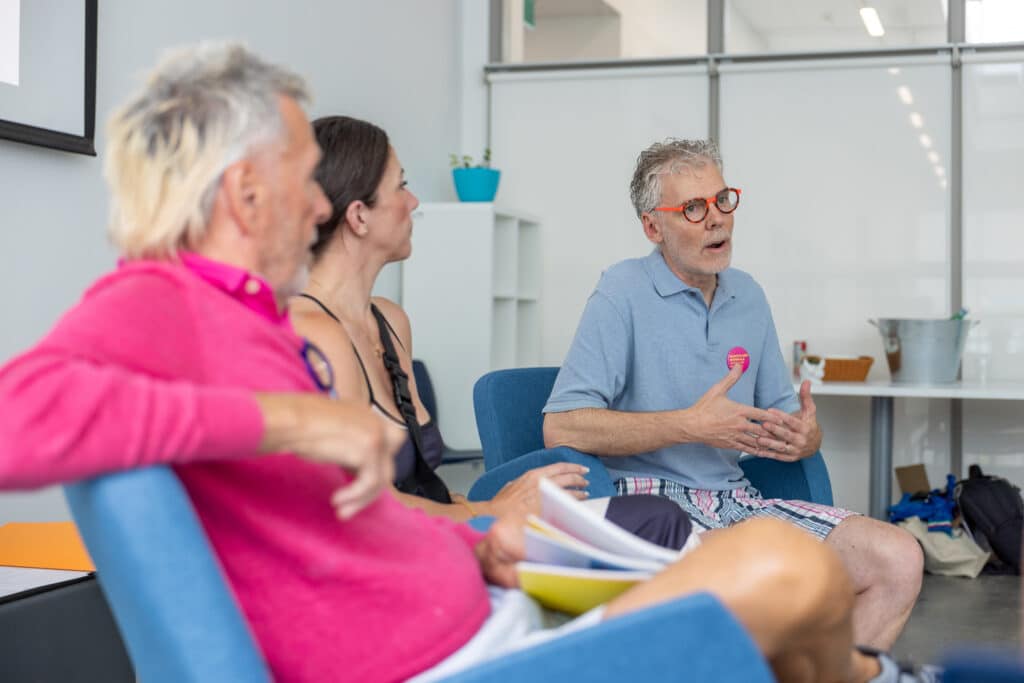A person in a pink top looks over to two people discussing