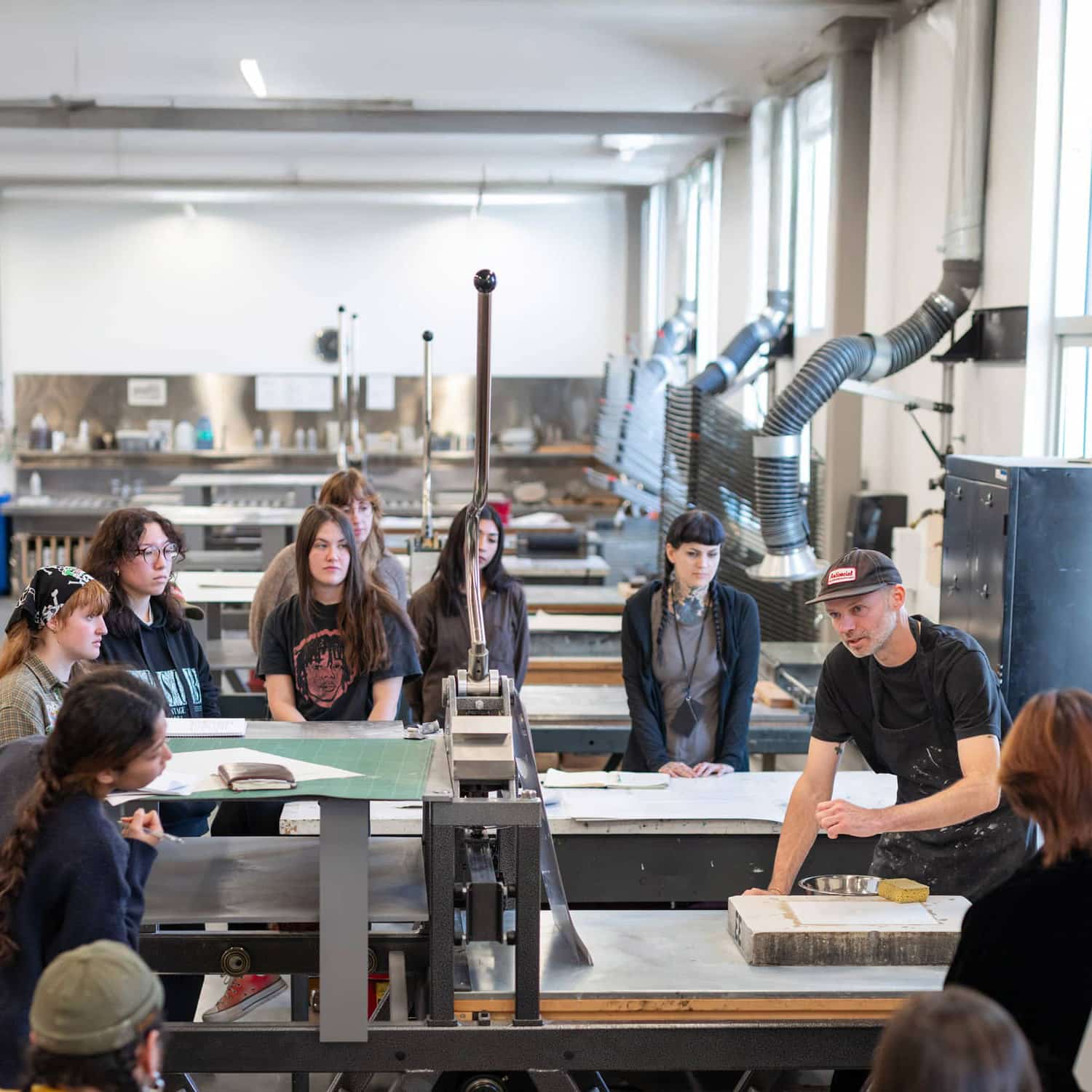 Hands-on learning in action. An instructor demonstrates traditional printmaking techniques to a focused group of students in Emily Carr University of Art + Design's vibrant print studio. Photo by Martin Dee