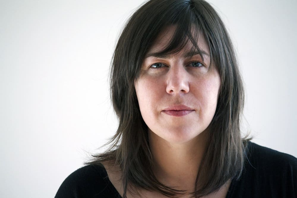 Portrait of a person with shoulder-length dark hair against a plain light background.