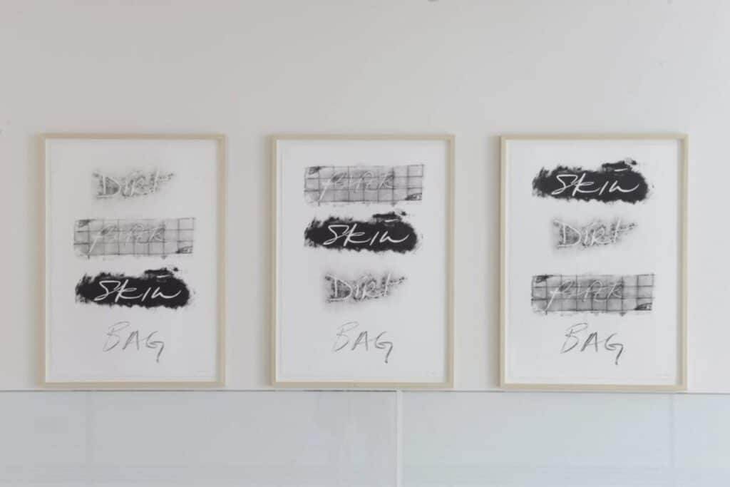 Three framed text-based artworks displayed side by side on a white gallery wall.