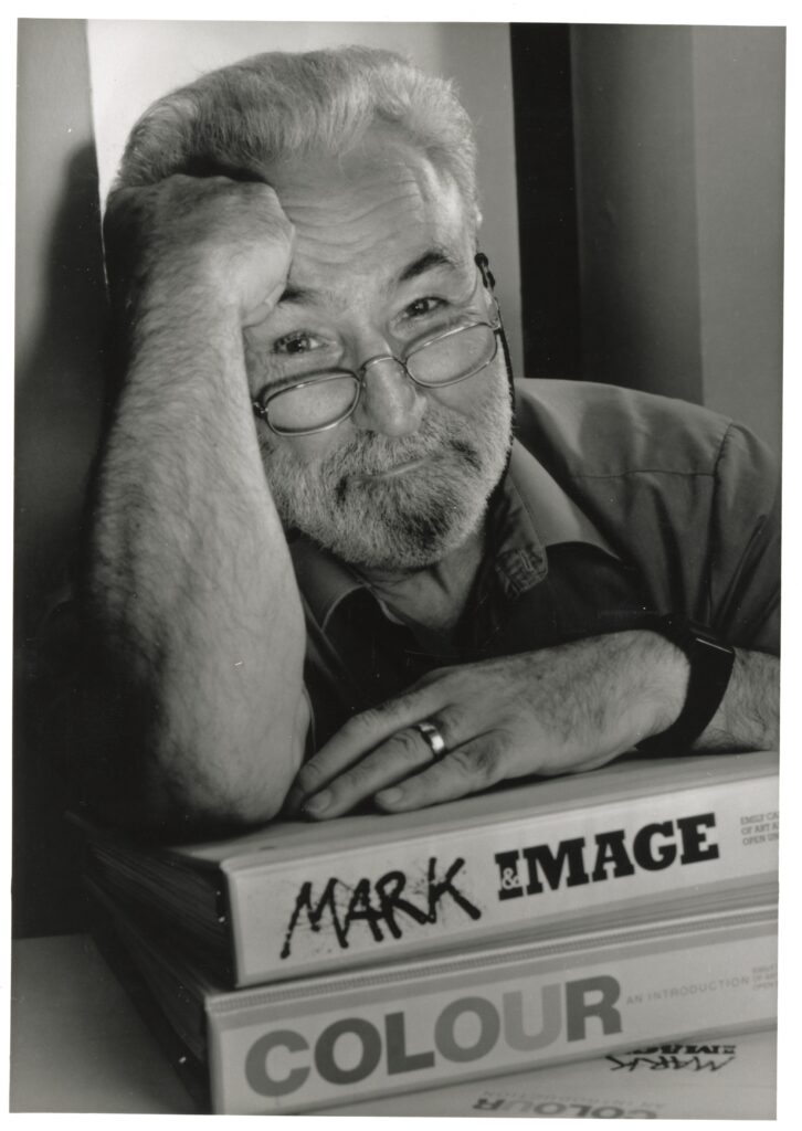 A photo headshot of a man leaning onto two course binders displaying the name "Mark and Image" and "Colour" 