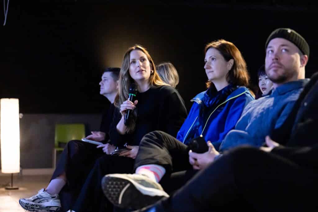 A group of audience members sit in rows, one person holding a microphone while others listen attentively under warm, focused lighting.
