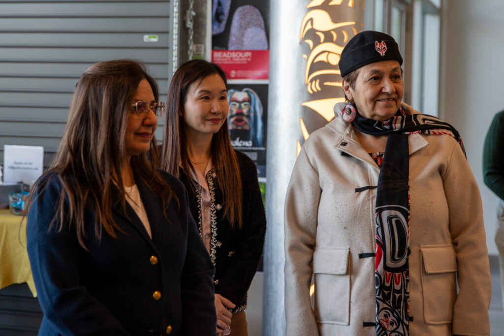 Three people stand side by side listening attentively in an indoor space with posters and displays.