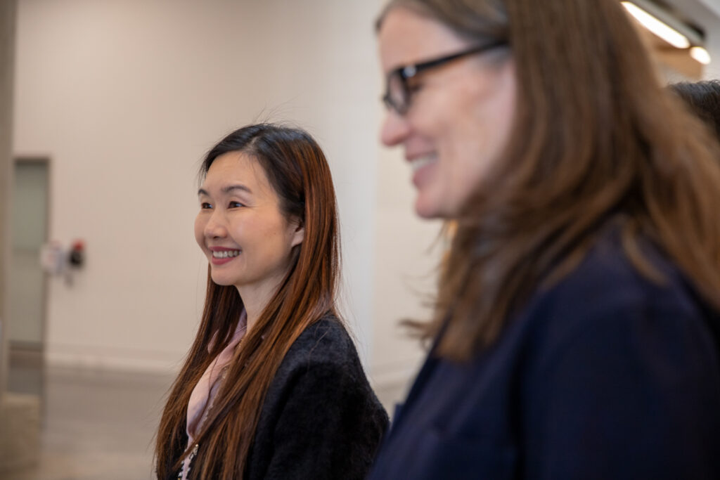 Two people smile while standing indoors during a conversation.