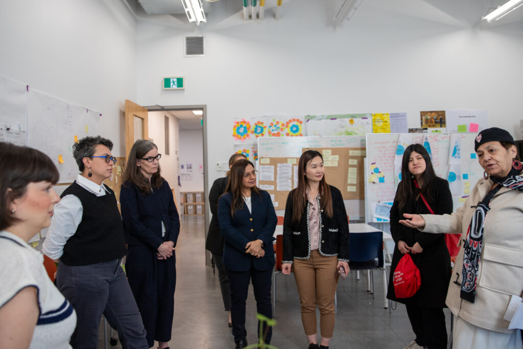 A group gathers in a classroom or studio while one person gestures during a discussion.
