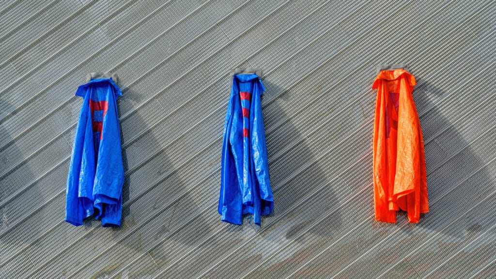 Three plastic garments in blue and orange hang against a textured wall, their surfaces creased and catching the light.