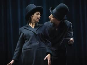 A still from the dance performance Show Gone, depicting two people wearing black suits and tall bowler hats.