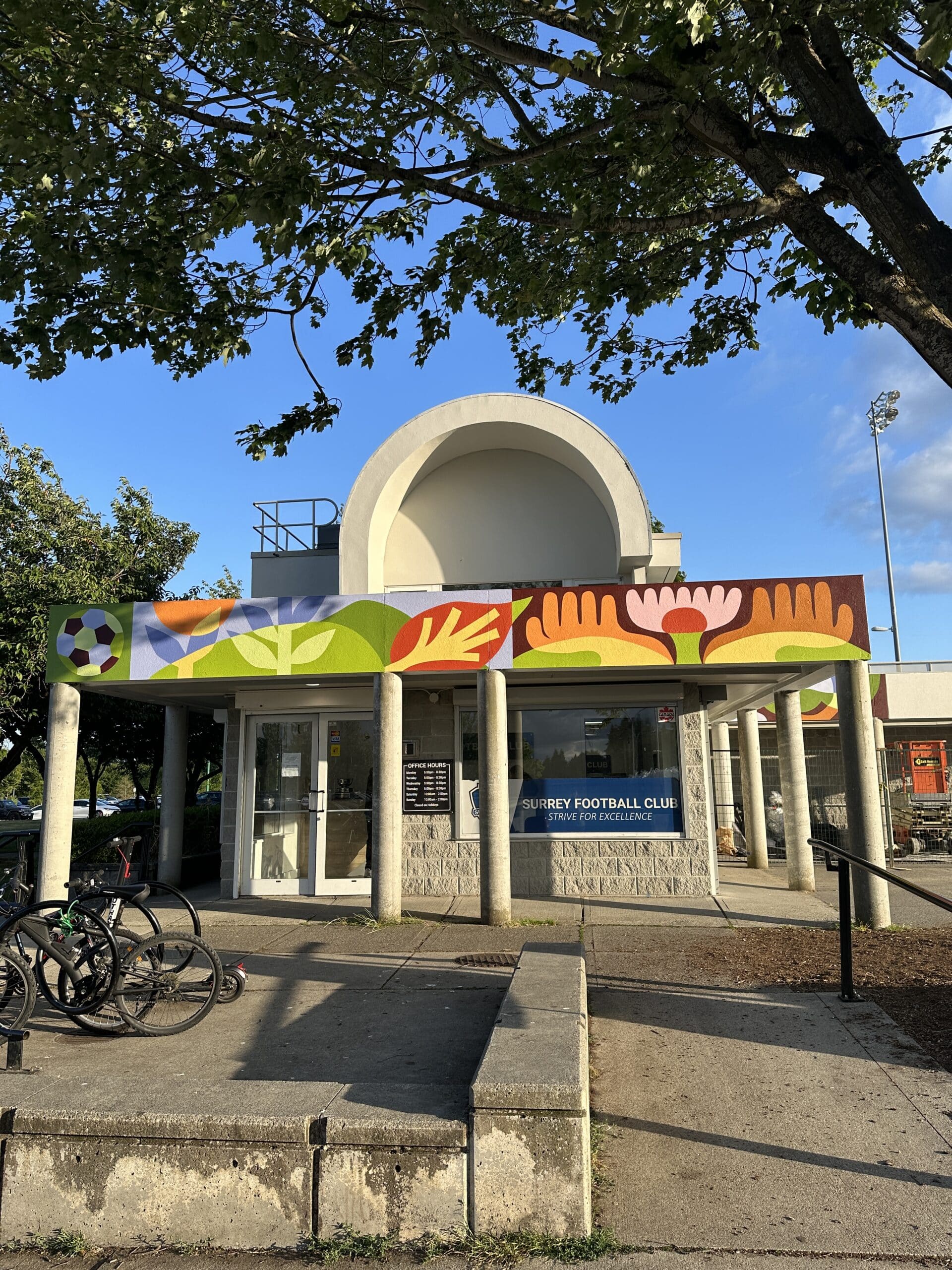 Front entrance of a community building with a colourful horizontal mural band above the doors, incorporating leaves, flowers and geometric patterns.