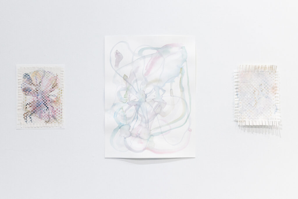 Three abstract artworks hang on a white wall, including two woven paper pieces and a large central painting in soft pastel tones.