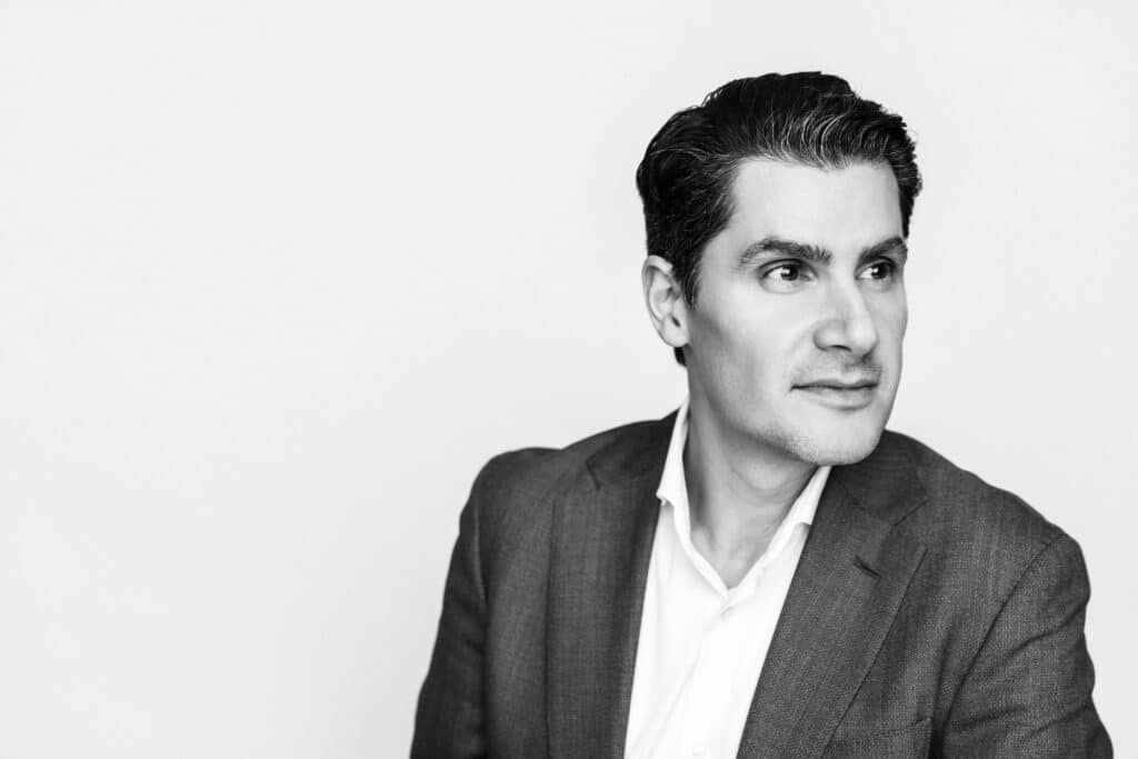 Black-and-white portrait of a person in a tailored jacket, gazing slightly to the side with a calm, reflective expression against a soft, light background.