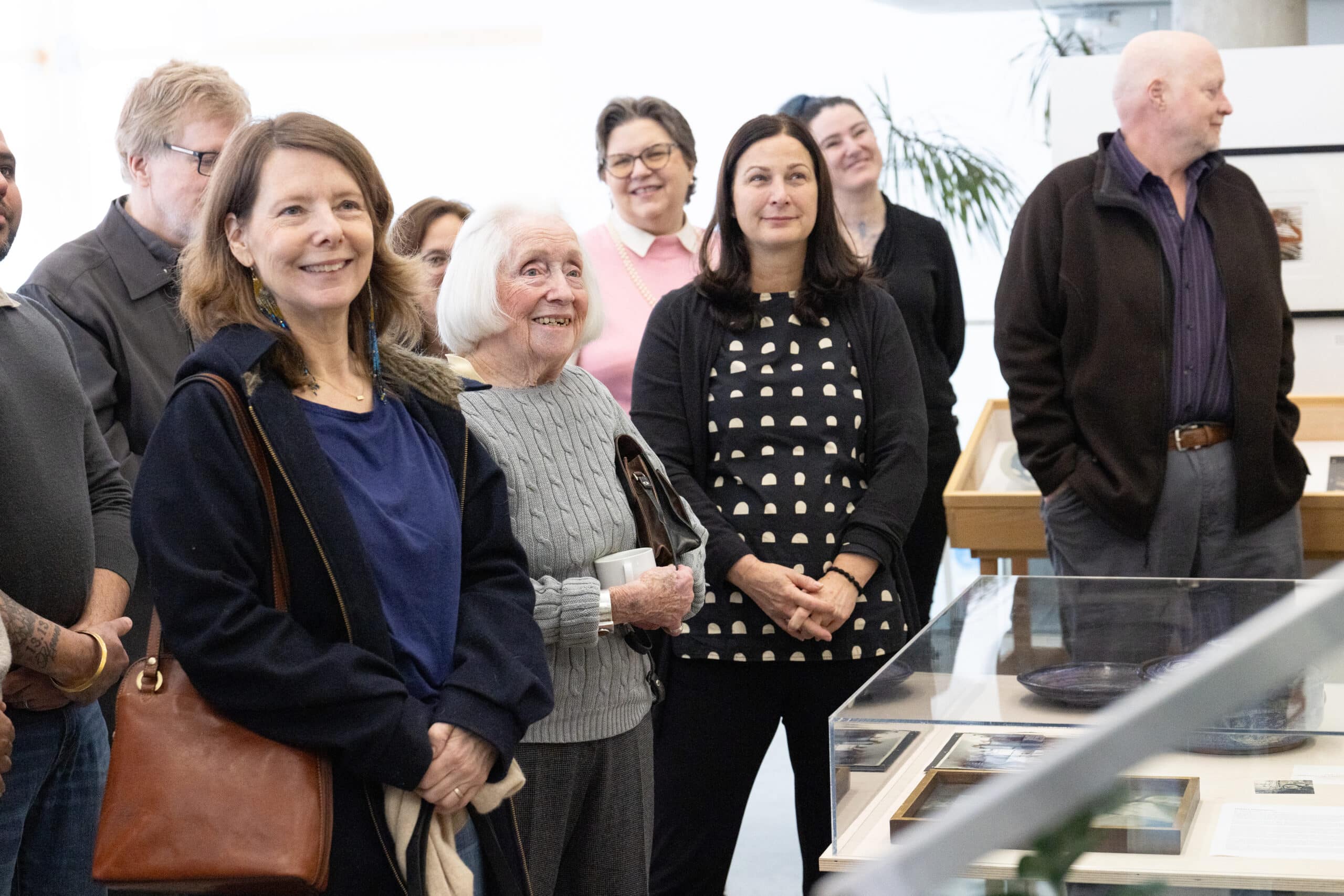 Visitors stand together listening attentively while facing a display case in an exhibition space.