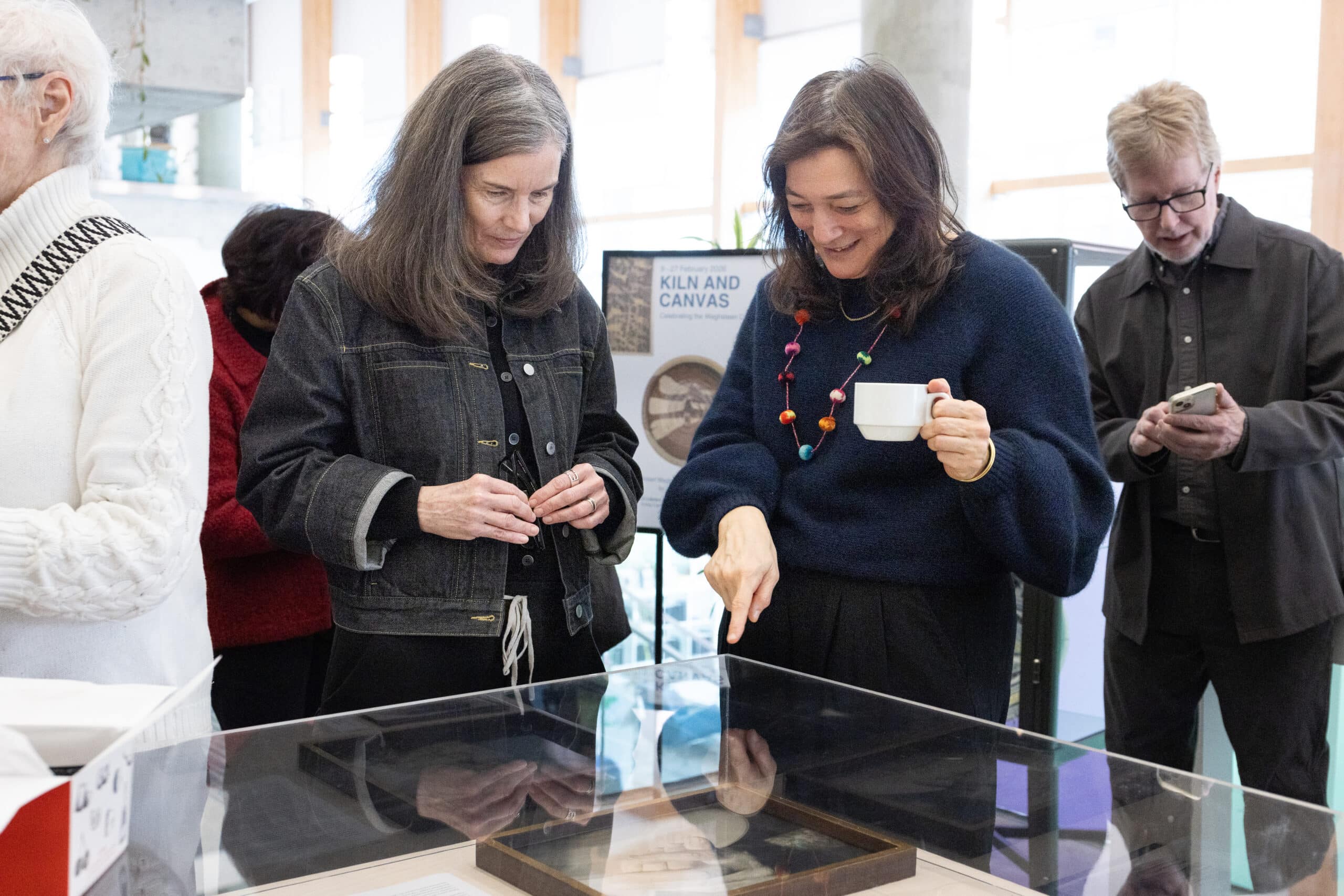 Two visitors stand beside a glass display case, one pointing at an item inside while others look on in the gallery.