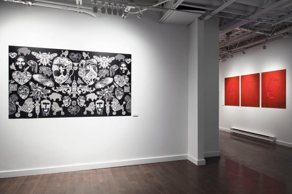 Inside a white gallery, a large black-and-white artwork filled with layered symbols stretches across the wall, while three red-toned pieces glow softly in a neighbouring room beyond a dividing pillar.