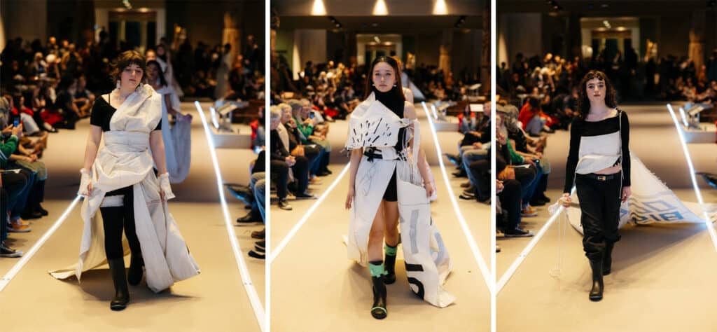 A model steps forward wrapped in flowing white fabric tied and folded across the body, the material shifting gently with each step.