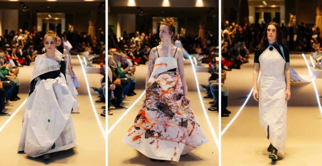 A model steps forward wrapped in flowing white fabric tied and folded across the body, the material shifting gently with each step.