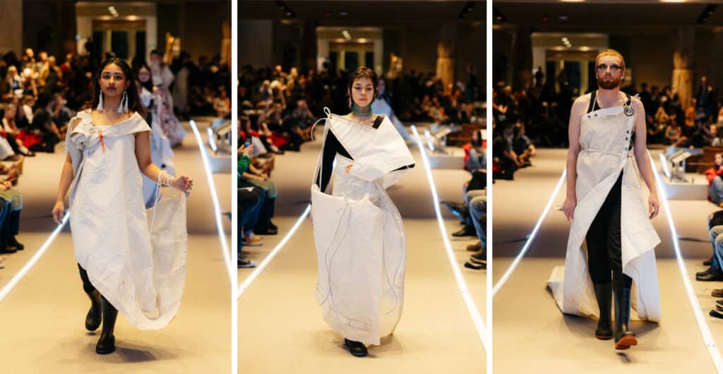 A model steps forward wrapped in flowing white fabric tied and folded across the body, the material shifting gently with each step.