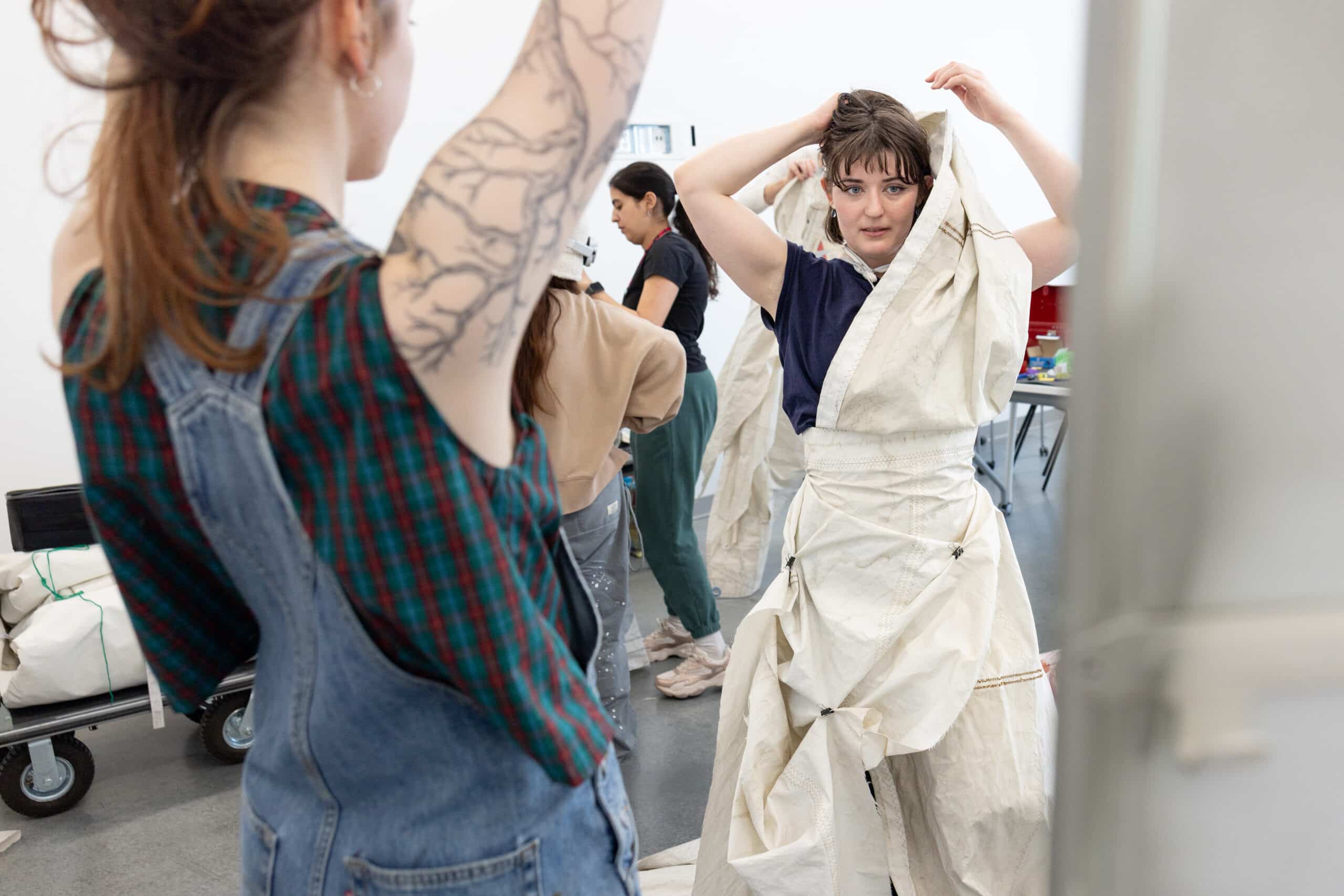 A person lifts a garment into place while another looks on, the moment balancing effort and ease.