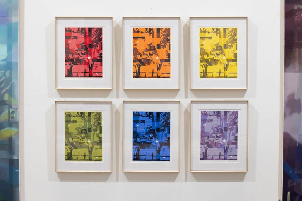 Six framed prints in shifting colours hang in a grid on a white gallery wall, each echoing the same layered image in a different hue.
