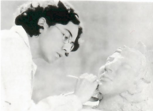 A black and white photo of a woman with a short haircut painting a sculptural piece