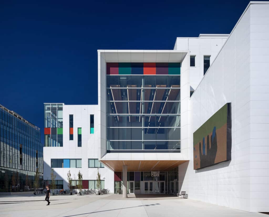 East entrance of Emily Carr University of Art + Design, showing the glass atrium, white exterior and colourful window panels on a clear day.