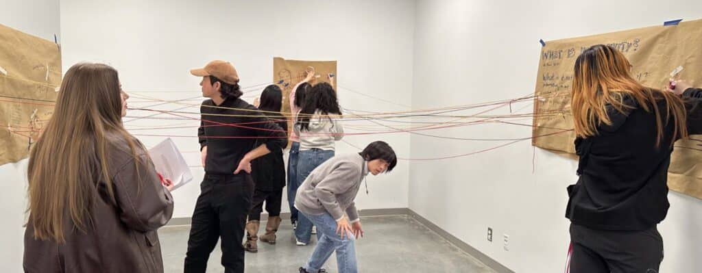Students connect ideas with coloured string between large paper displays during a collaborative classroom installation.