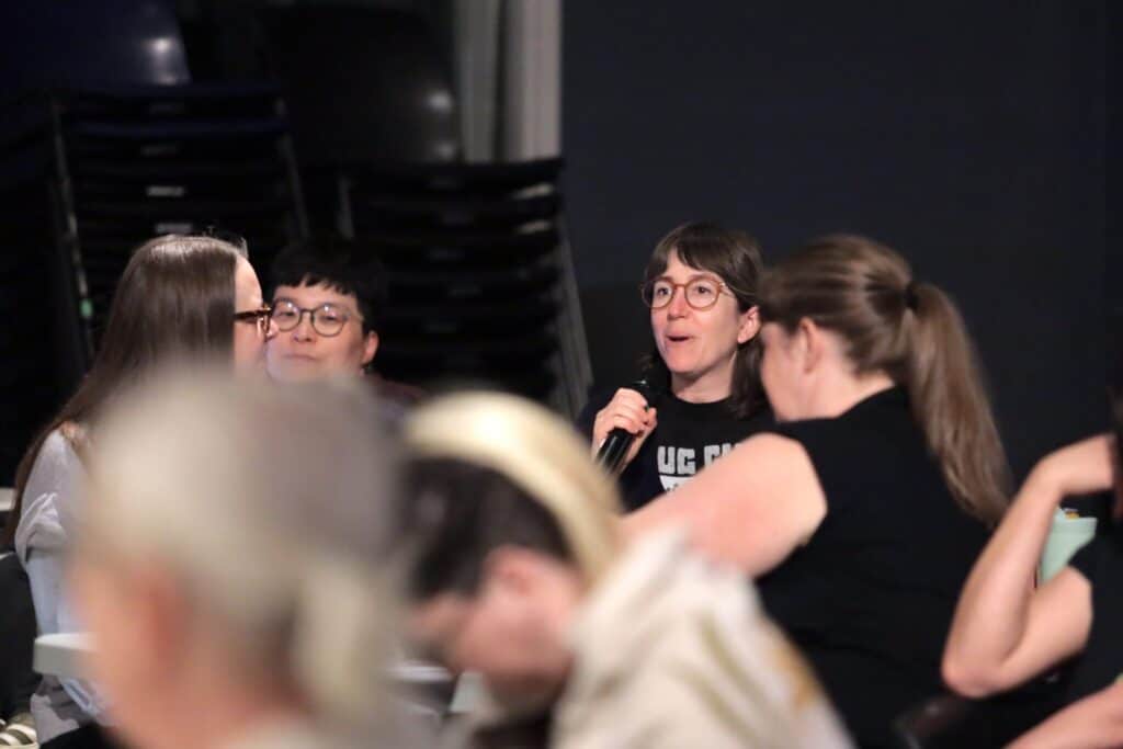 A participant speaks into a microphone during a group discussion while others listen and take part in a professional learning session.