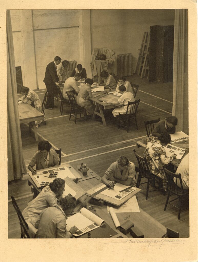 Students working at large tables in an art classroom, viewed from above.