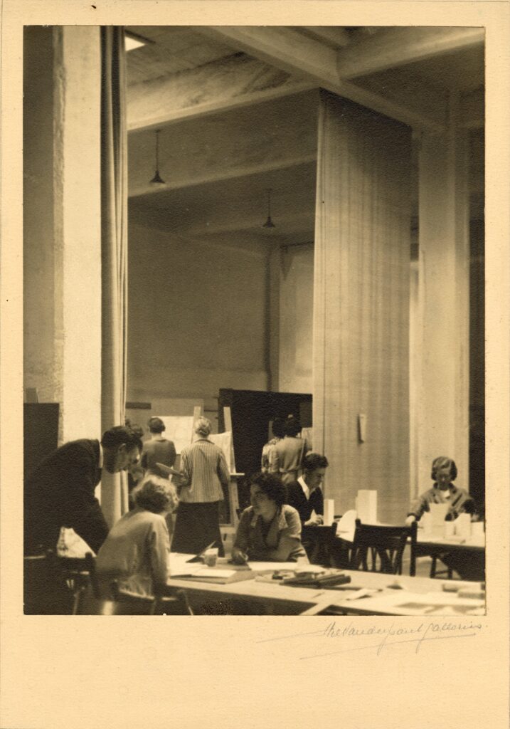 Students working at tables and easels in a large art classroom.