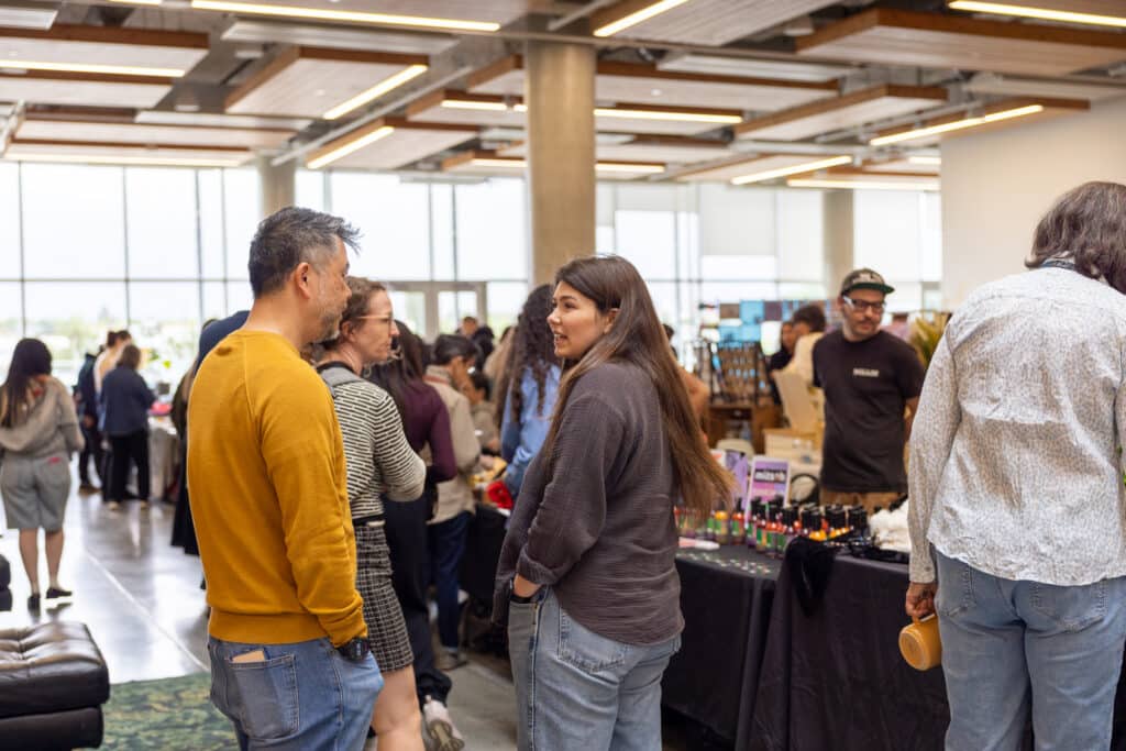 People browsing and talking with vendors at a busy indoor market.
