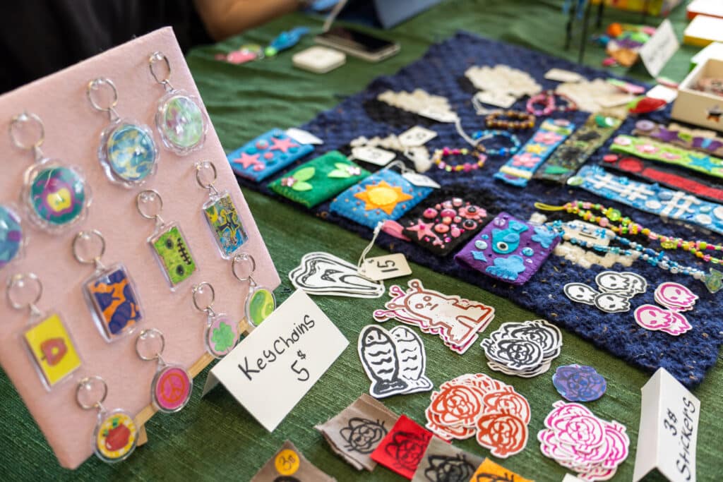 Handmade keychains, stickers, bracelets and other colourful goods displayed for sale on a table.