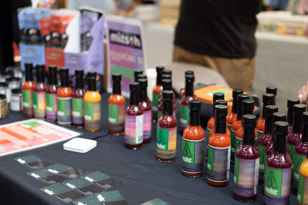 Bottles of colourful hot sauce displayed for sale on a vendor table.