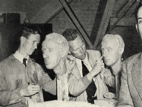 Two people adjusting face sculptures with a person on the right touching the cheek