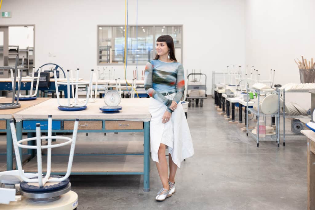 Person leans against a worktable beside a scale in a bright ceramics studio.