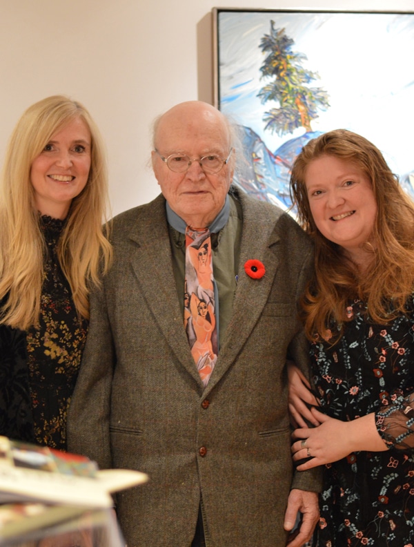 Three people pose together in front of a colourful painting in a gallery.